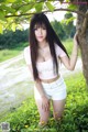 A young woman leaning against a tree in a field.