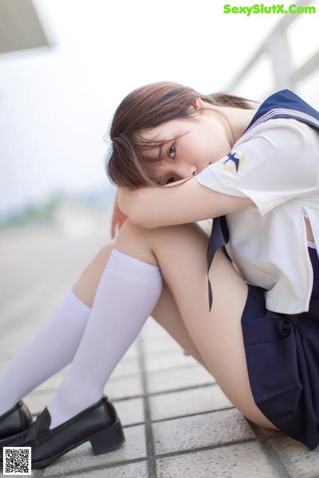 A woman in a school uniform sitting on the ground.