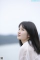 A woman with long black hair standing by the water.