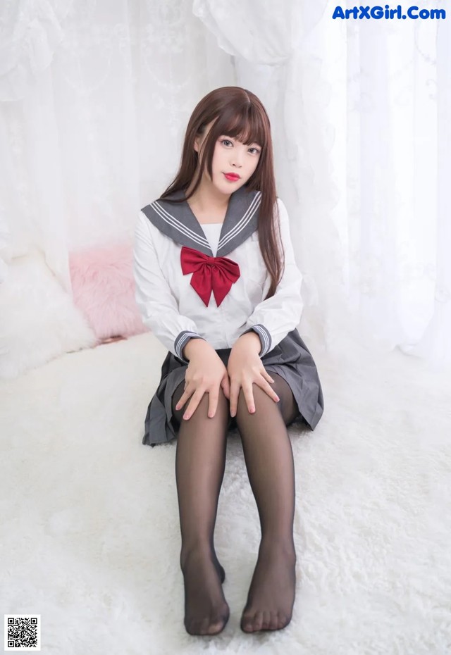 A woman in a school uniform sitting on a white rug.