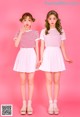 Two young women standing next to each other on a pink background.