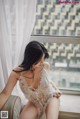 A woman in a white lingerie sitting on a window sill.