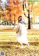 A woman in a white dress is walking through the leaves.