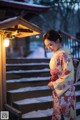 A woman in a kimono standing in front of a lantern.