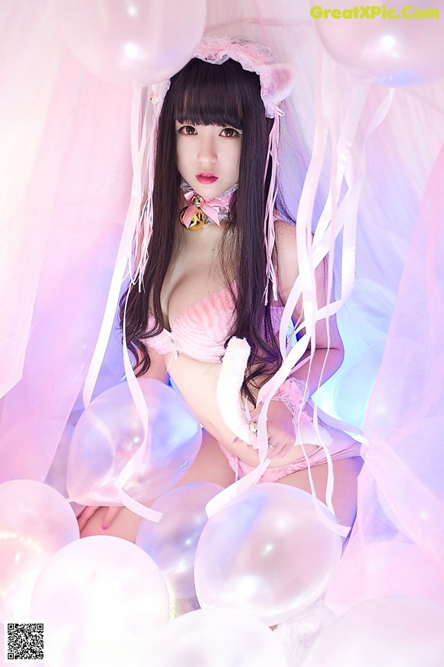 A woman in a pink lingerie sitting on a bed of balloons.