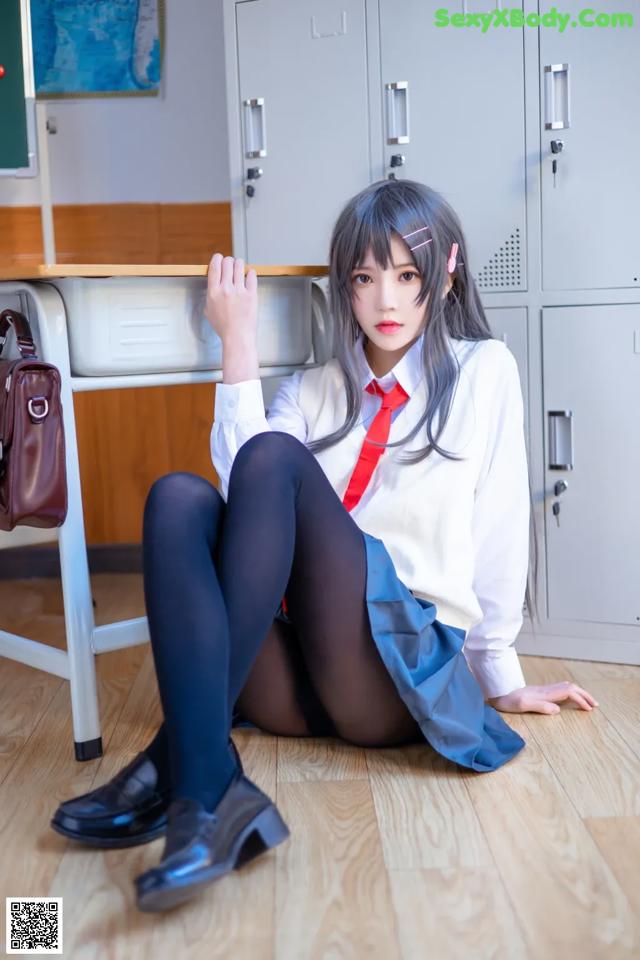 A woman in a school uniform sitting on the floor.