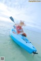 A woman in a straw hat paddling a blue kayak in the ocean.