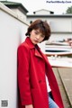 A woman in a red coat leaning against a wall.