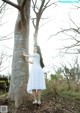 A woman in a white dress leaning against a tree.