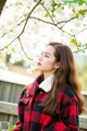 A woman in a red and black plaid coat standing under a tree.