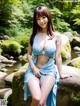 A woman in a blue dress sitting on a rock by a river.